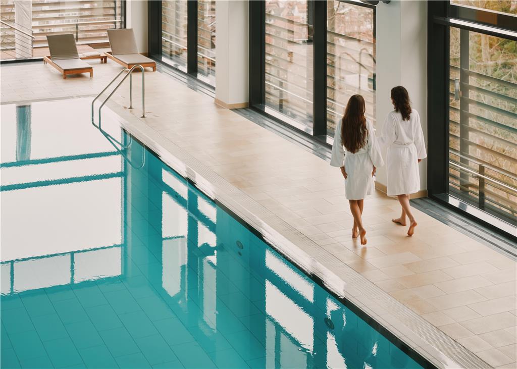 Two guests in bathrobes walking next to the indoorpool