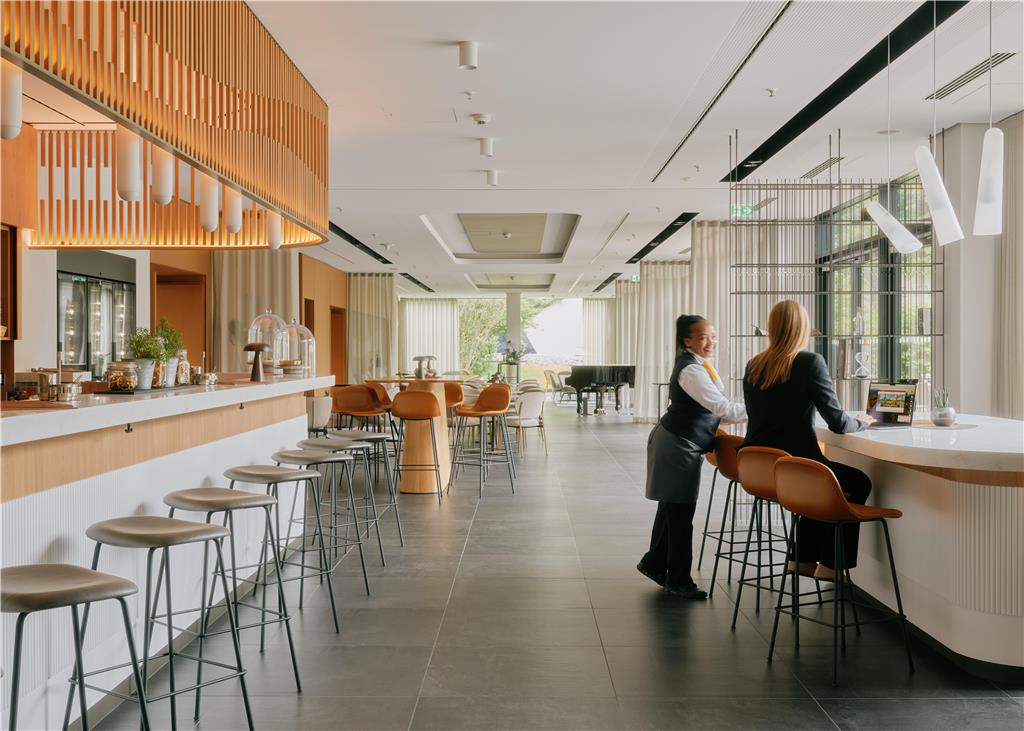 All-day bar with terrace. An employee serves a guest. There is a piano in the background.